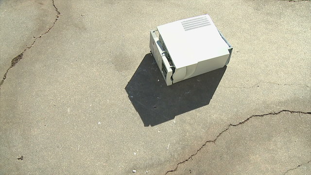Computer Shutdown Fail. An old personal computer is dropped onto concrete and breaks apart. Shot in slow motion at 60fps.