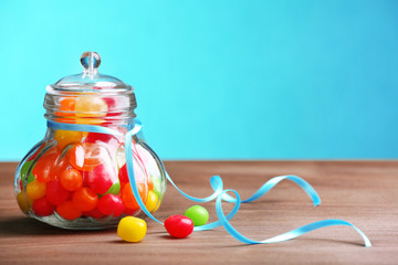 Colorful candies in jar on table on blue background