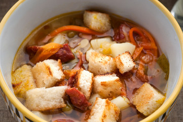 Soup with croutons, peas, carrot and tomatoes close up