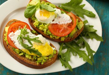 Tasty sandwiches with egg, avocado and vegetables on plate, on wooden background