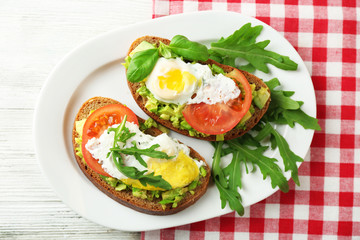 Tasty sandwiches with egg, avocado and vegetables on plate, on wooden background