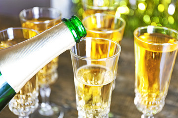 Pouring champagne from bottle into glasses on bright background