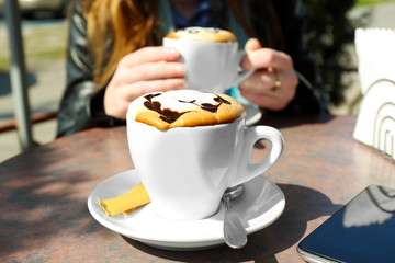 Hands holding cup of cappuccino in cafe, outdoors