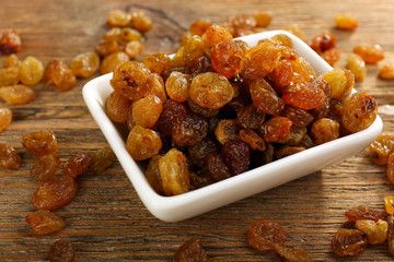 Raisins in saucer on wooden table, closeup