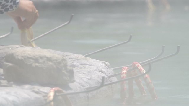 prople hanging a eggs basket on hook in hot water from hotspring