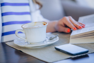 beautiful young girl in outdoor cafe reading a book and drinking