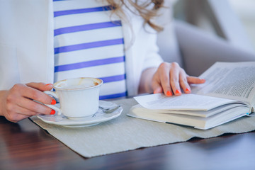 beautiful young girl in outdoor cafe reading a book and drinking