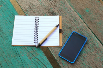 notebook with pen and mobile phone on the green table