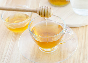 Pouring honey into cup of tea on wooden table