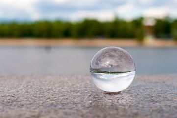 Fototapeta na wymiar Glass transparent ball on river background and grainy surface