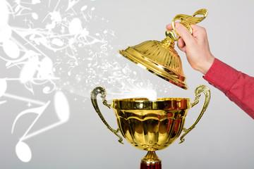 Hand opens the lid of the golden cup with a musical key