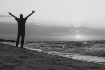 Monochrome image. Man welcomes the sunrise on beach