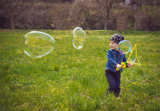 Cute Little Boy In Texas Clothes Is Playing In The Park With Big Blowing Bubbles