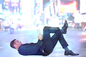 Composite image of businessman lying on the floor reading book 