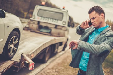 Man calling while tow truck picking up his broken car