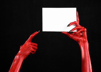Red devil hand with black nails holding a blank white card