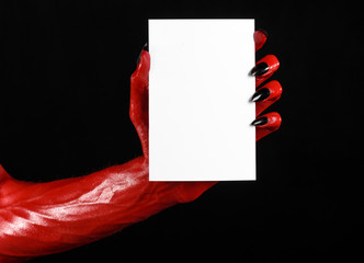 Red devil hand with black nails holding a blank white card