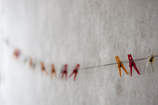Coloured plastic clothes pegs on a washing line against a whitewashed wall.
