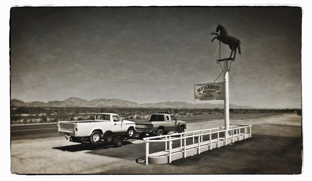 A truck towing a trailer parked at a roadside stop on a desert highway. 