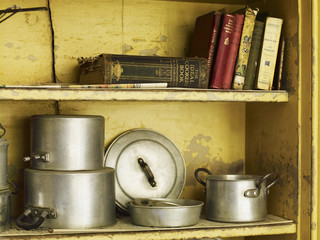 Old well worn recipe books and pots and pans on a kitchen shelf.
