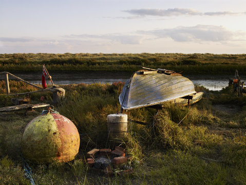 An upturned fishing boat by a narrow water channel in a flat landscape. Fishing floats and buoys.