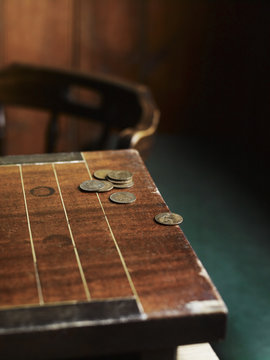 A pub games table with copper coins laid on the surface. A traditional carved chair.