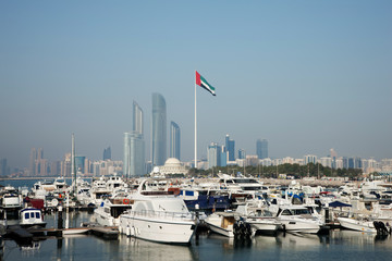 City skyline with the national flag and boats moored in the marina, Abu Dhabi, UAE
