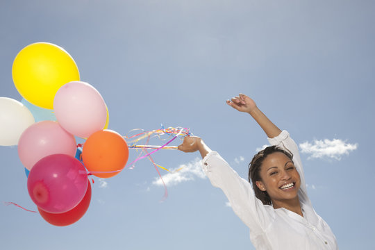 Smiling woman with her arms in the air holding a bunch of multi coloured balloons
