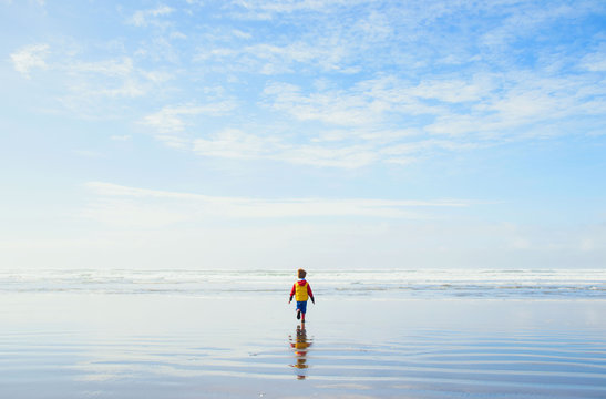 Rear view of a boy in a raincoat and wellies on the beach walking towards the sea, USA