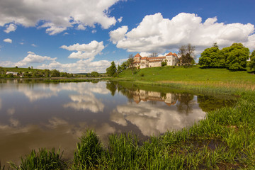 old castle and green reflection in blue water with cloudy sky background