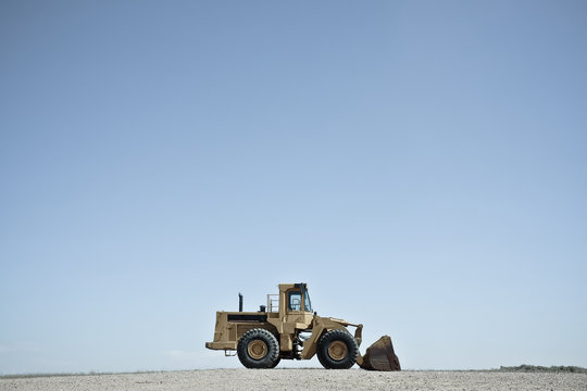 Side view of a Bulldozer parked on a gravel road against a blue sky, Wyoming, USA