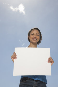 Smiling woman standing outdoors in front of a blue sky holding a blank pice of card