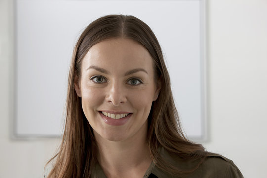 Close-up portrait of a smiling businesswoman standing in front of a whiteboard in an office