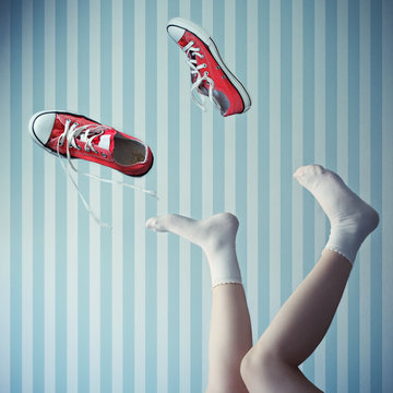 Close-up of a girl lying on her back with her legs in the air kicking off her canvas shoes