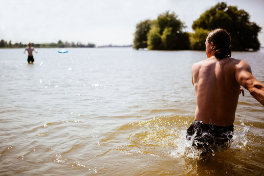 Man standing in a lake throwing a plastic frisbee to his friend, IJsselmeer (Lake IJssel), Netherlands 