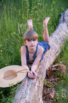 Young boy wearing blue overalls laying on fallen tree