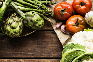 Close-up of fresh artichokes, cauliflower, asparagus, tomatoes and garlic on a wooden table