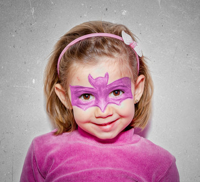 Portrait of a smiling girl in pink with a bat mask drawn on her face