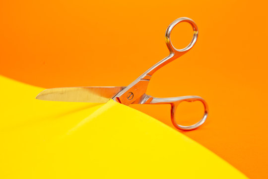 Close-up of a pair of Scissors Cutting a piece of Yellow Paper with an orange background