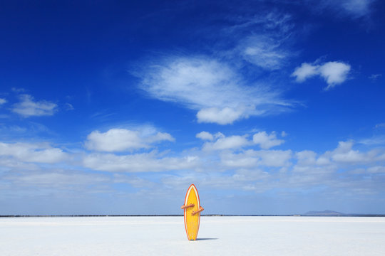Woman hiding behind and holding a surfboard upright on a sandy beach, Cummins, South Australia, Australia