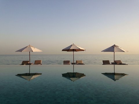 Reflections of Three Parasols and six sun loungers on a beach by a swimming pool 
