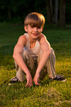 USA, Pennsylvania, Lancaster County, Lancaster, Portrait of blond boy (8-9) squatting on ground at sunset
