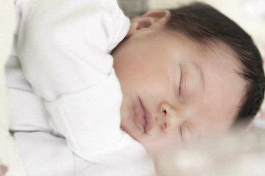 Close-up of a newborn baby boy with brown hair lying on his side sleeping 