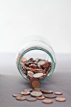 Close-Up of coins spilling out of a glass jar onto a table