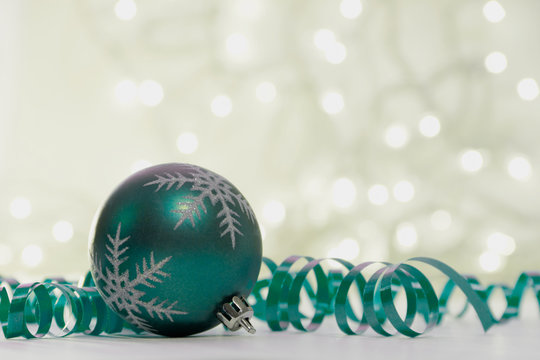 Close-up of a green Christmas bauble with a snowflake pattern with party streamers and illuminated fairy lights on a table