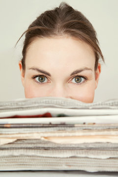 Young woman peeking over the top of a stack of newspapers