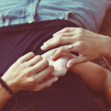 Close-up of a man lying on the grass stroking a woman's hand