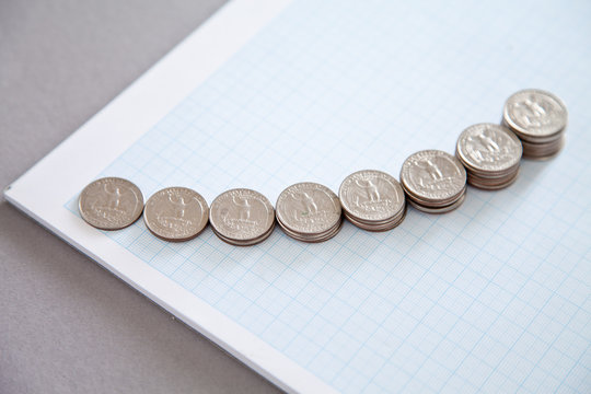 Overhead view of Stacks of US Quarter coins arranged in an ascending curve on blank graph paper