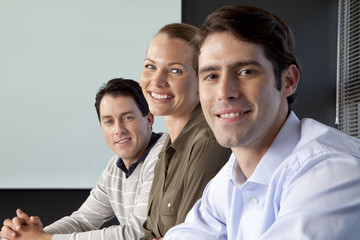 Three smiling business people sitting side by side at a meeting table in an office