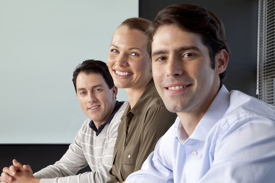 Three smiling business people sitting side by side at a meeting table in an office